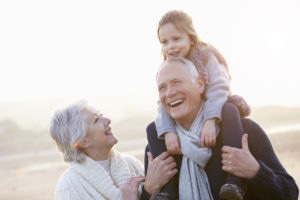 Grandparents And Granddaughter Walking On Winter Beach Laughing